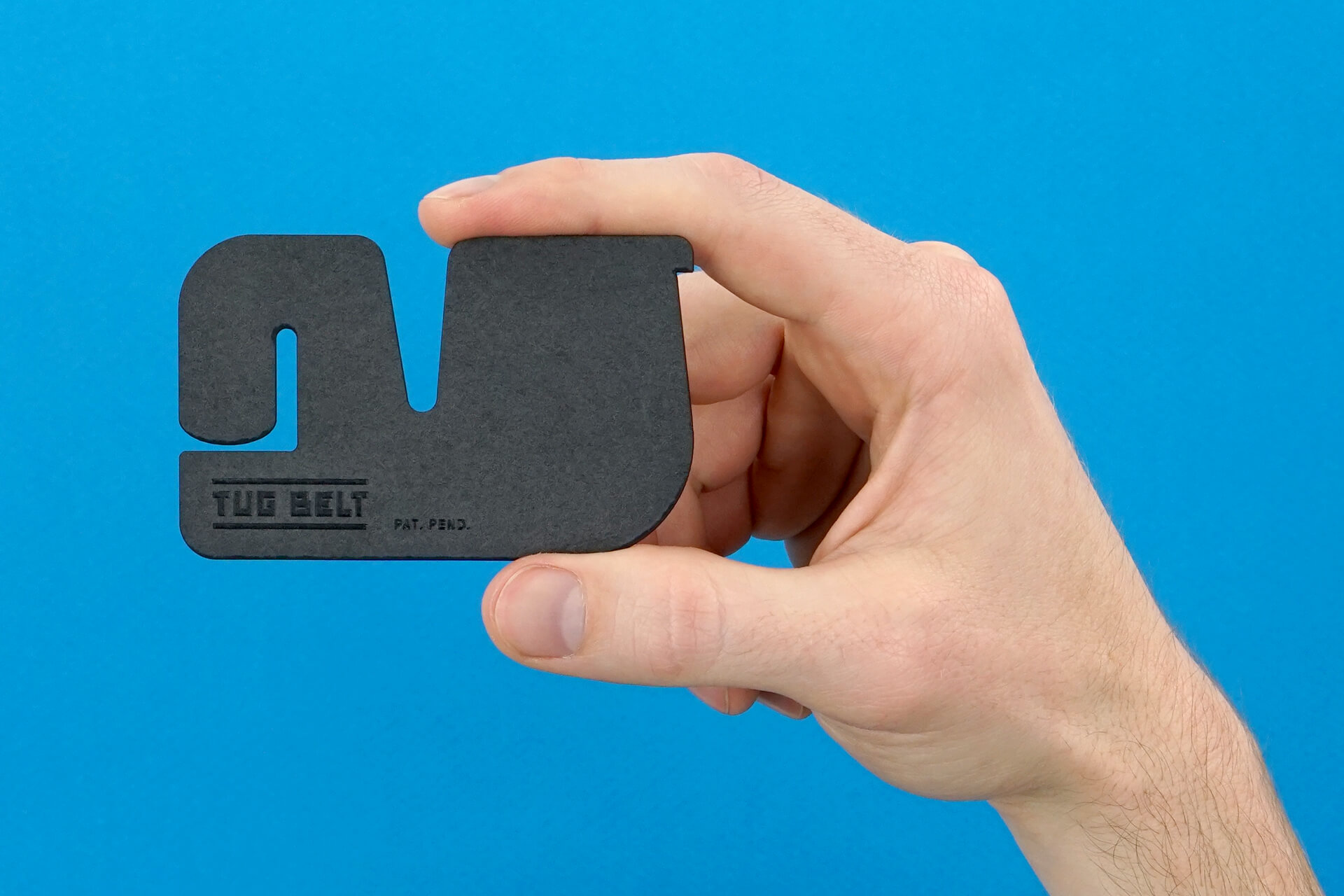 The TugBelt, a minimalist belt the size of a credit card, being held up in front of a blue backdrop.